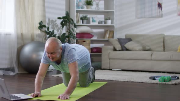 Elderly Man Practicing Yoga with Laptop at Home alt