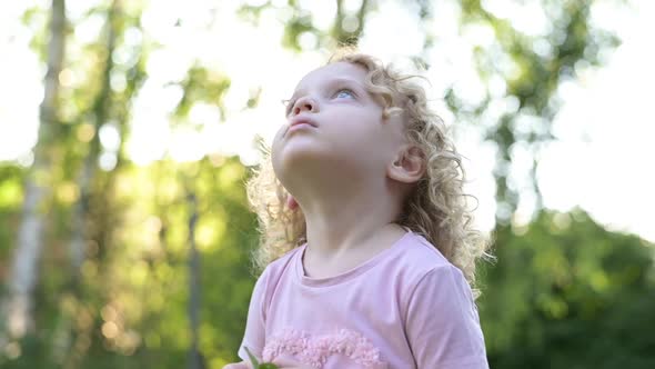 Portrait of a little beautiful curly-haired girl who looks into the sky alt