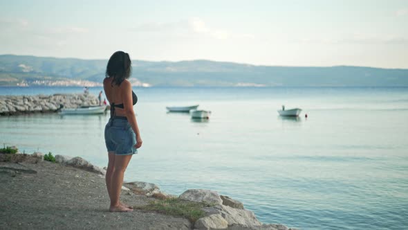 A Dreamy Romantic Girl Looks at the Ocean Water During a Walk alt