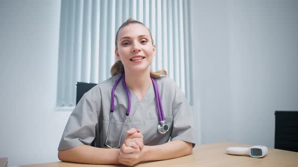 Woman Doctor Sits at Workplace Looks at the Camera and Communicates with the Patient Via Video Call alt