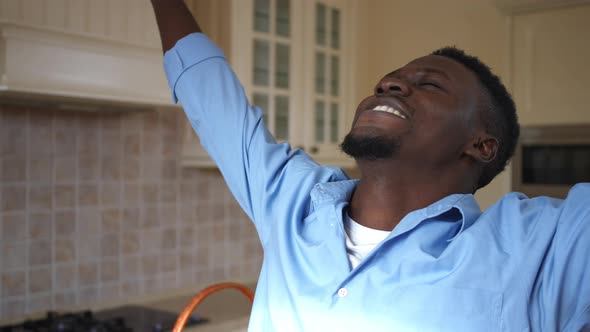 Excited Satisfied Young Man Stretching Hands Standing in Kitchen at Home Indoors alt