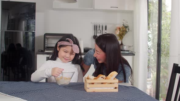 Asian mom and daughter feeling happy talking together while eat bread, corn flakes. alt