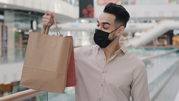 Young Guy in Medical Mask Holding Shopping Bags Showing Thumb Up Satisfied Services Arab Man alt