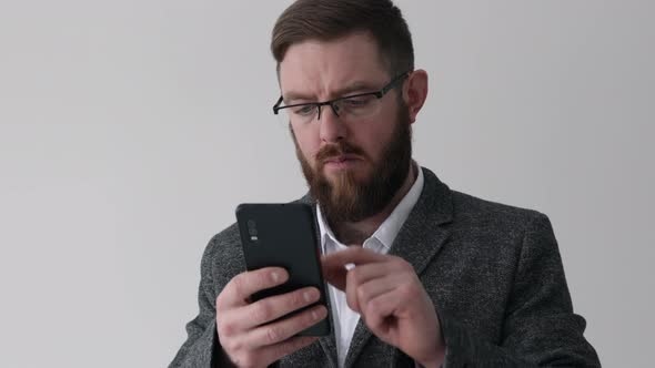 Close up view of bearded middle aged man using phone on the white wall background texting message