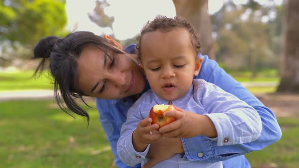 Mixed-race Pretty Mother Hugging Son, Looking Him Eating Apple alt