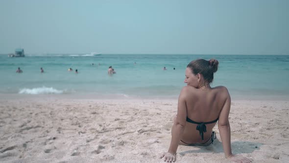 Slim Girl Lies on Yellow Sandy Beach Against Blue Ocean alt