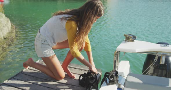 Side view of a teenage Caucasian girl untying a rope on the boat harbor side alt