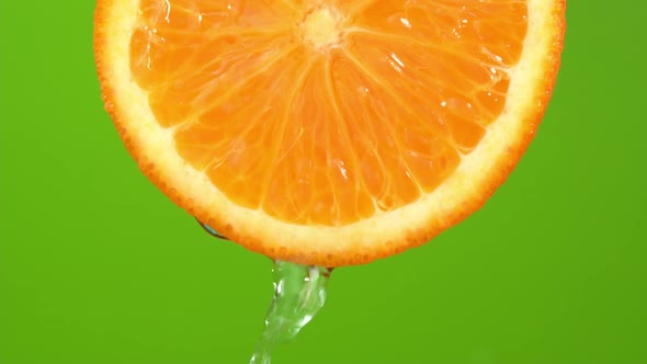 Water falling from orange hue orange on green background. Orange slice and water splashing, drops alt