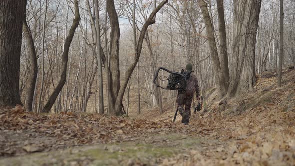 Gimbal following bowhunter in camouflage outfit walking in forest path during winter alt