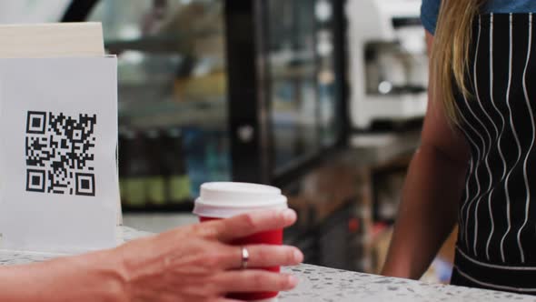 Mid section of woman wearing face mask making payment using smartwatch at a cafe alt