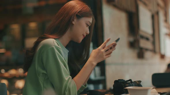 Young Asian woman using smartphone browsing the internet chatting on a phone sitting at coffee shop