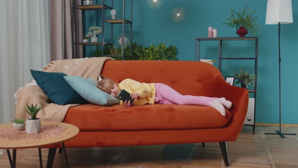 Child Toddler Hold Smartphone Watching Online Cartoons Chatting with Friends on Sofa Alone at Home alt