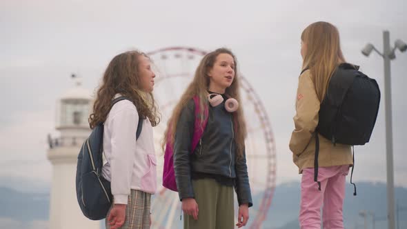 Three School Girlfriends Hang Out After Classes Near Luna Park with Ferris Wheel
