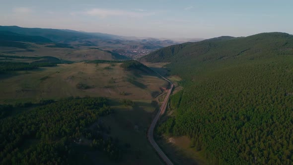 AERIAL, TOP DOWN: Dark Colored Car Driving Down an Asphalt Road Crossing the Vast Forest on a Sunny alt