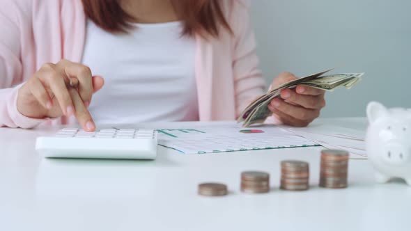 Young woman calculating expenses with stack of coins and piggy bank