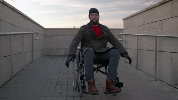 Happy Disabled Man in Wheelchair is Rolling Down Handicapped Ramp on City Street alt