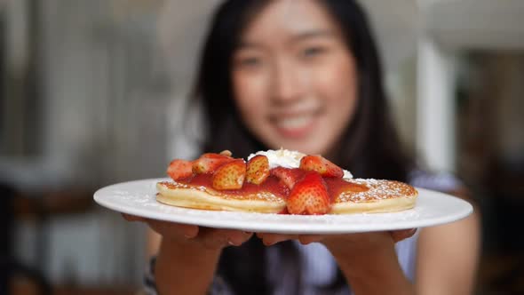 Young Asian woman holding a dish with breakfast of pancakes.