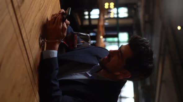 Vertical Shot of Confident Young Man in Suit Using Smartphone During Waiting for Girlfriend Sitting alt
