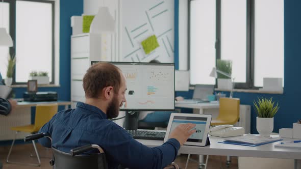 Businessman with Disabilites Using Computer and Tablet Comparing Graphs alt