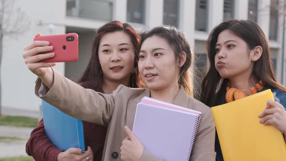 Asian college students taking a selfie with a mobile phone while standing outside the university alt