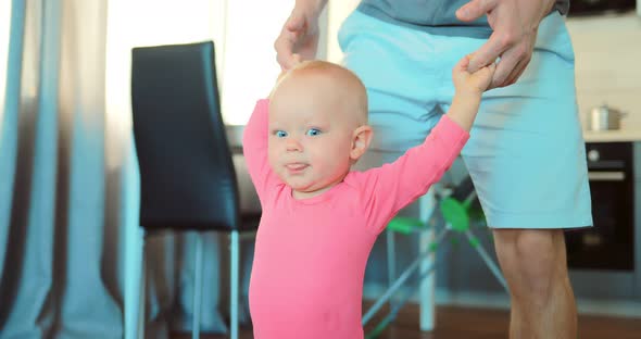 Child Holds Hands with His Father and Takes the First Steps alt