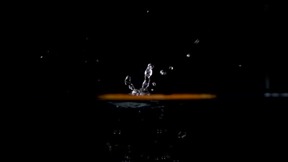 high speed camera slow motion reverse video of an orange slice splashing into the water. Black backg alt