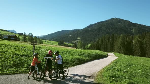Three cyclist looking at map in landscape, Alta Badia, Italy