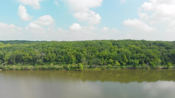 drone flight right of a tree line in thick green forest with blue sky and white clouds on summer sun alt
