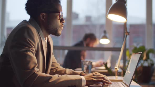 Afro-American Male Office Worker Using Laptop at Desk in the Evening alt