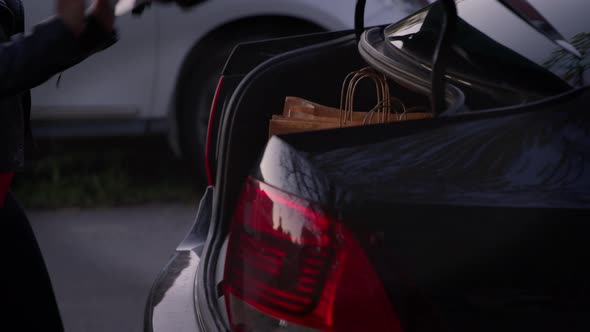 Beautiful Girl Pulls Out Shopping Bags From Car Trunk. alt