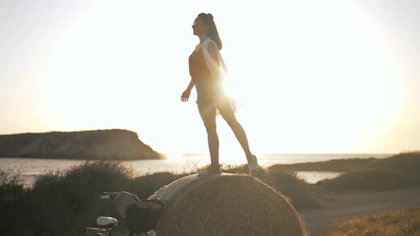 Slim Happy Woman Imitating Flying Bird Standing on Yellow Pile of Wheat in Sunbeam alt