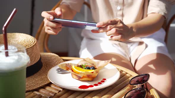 Young woman taking photo of dessert with smart phone for social media in restaurant alt
