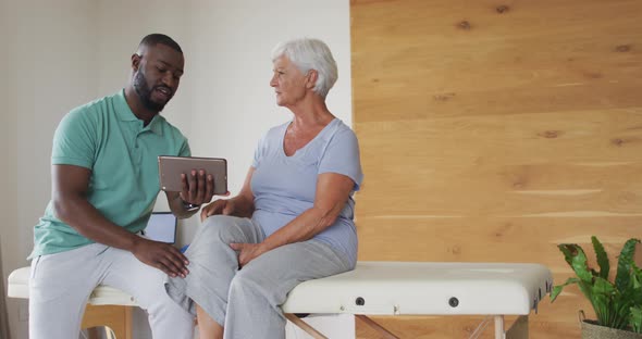 Video of african american male physiotherapist using tablet with caucasian senior woman alt