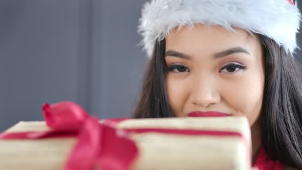 Closeup Attractive Young Asian Christmas Girl Wearing Santa Claus Hat Holding Gift Box with Red Bow alt
