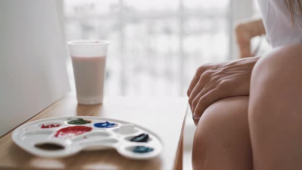 Artist Sits Near Palette with Paints and Cup on Wooden Easel alt