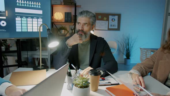 Zoomout of Businesspeople Talking Sitting at Desk in Boardroom Working at Night Together alt