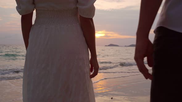 Young woman traveler holding man's hand and looking beautiful sunset on the beach
