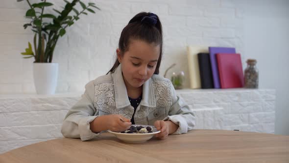 Closeup of a Cute Baby Girl with Pleasure and Appetite Picks Up Raspberries Blueberries and Puts alt