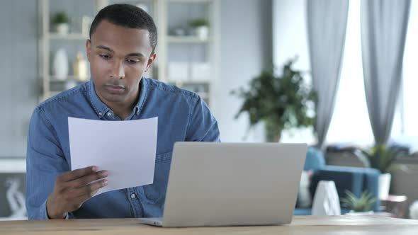 Young African Man Working on Documents and Laptop in Office alt
