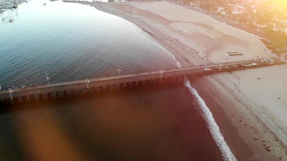 Aerial drone shot over the beaches and tourists walking out on Stearns Wharf pier during a colorful alt