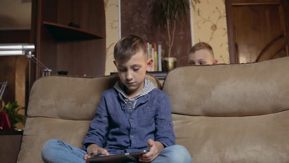 Boy Sitting on the Couch at Home and Uses Tablet PC to watch Video or Gaming alt