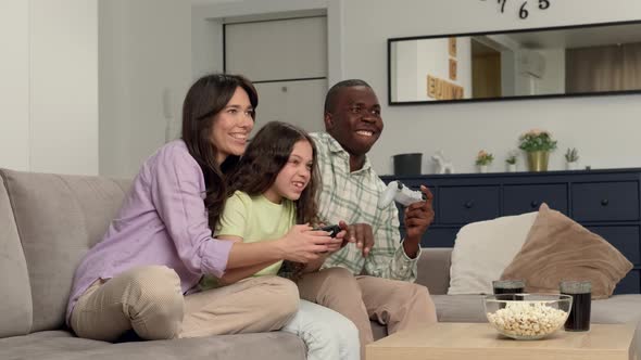 Multi Ethnic Family of Three Playing a Video Game at Home Sitting on the Couch alt