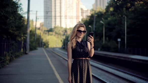 Woman Using Mobile Phone And Waiting Public Transport On Train Station. Active Lifestyle On Vacation alt