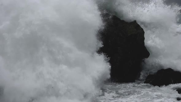 Slow motion of powerful waves crashing after hitting the rocks on the seashore. Close up. alt