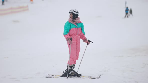 Happy Young Brunette Woman Standing on Skis Waving and Smiling alt