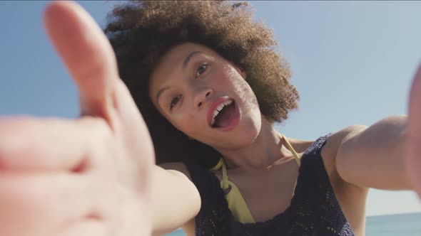 Mixed race woman sending kisses through camera at beach alt