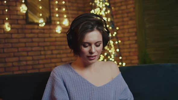 Smiling Girl Uses a Laptop Listens to Music in Headphones and Sings alt