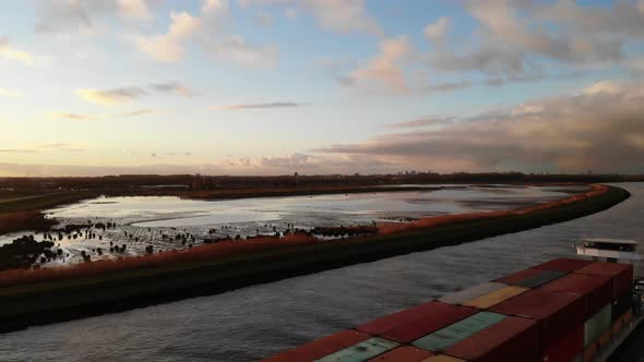 Fully loaded cargo vessel sailing with containers on the dutch river Noord while the sun gives the n alt