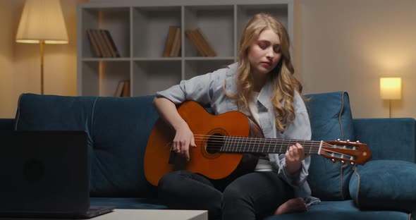 Thoughtful Young Woman Is Playing Sad Song on Guitar at Evening at Home Creative Hobby and alt