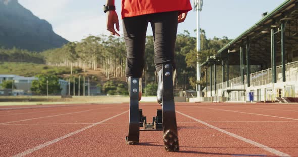 Disabled mixed race man with prosthetic legs walking on racing track towards starting blocks alt